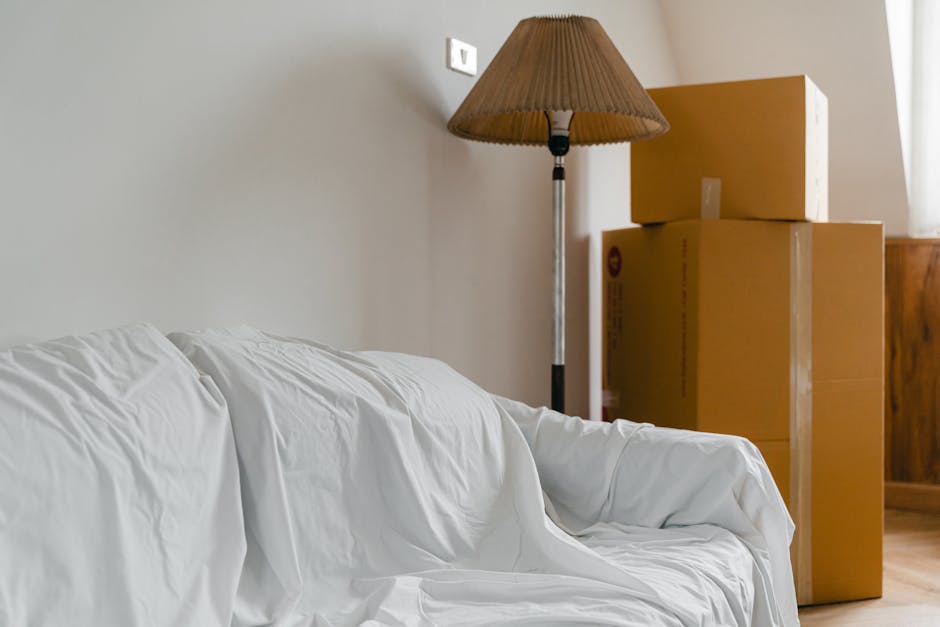 Inside a room during a house move, there are three cardboard boxes stacked on top of each other near the wall, with the largest box at the bottom and the smallest on top. The boxes are sealed with pac