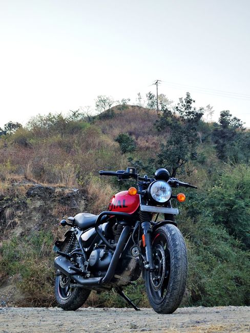 The image shows a black motorcycle parked on the side of a paved road, with urban street lights and power lines visible in the background. The motorcycle has a sleek design with a rounded headlight, r